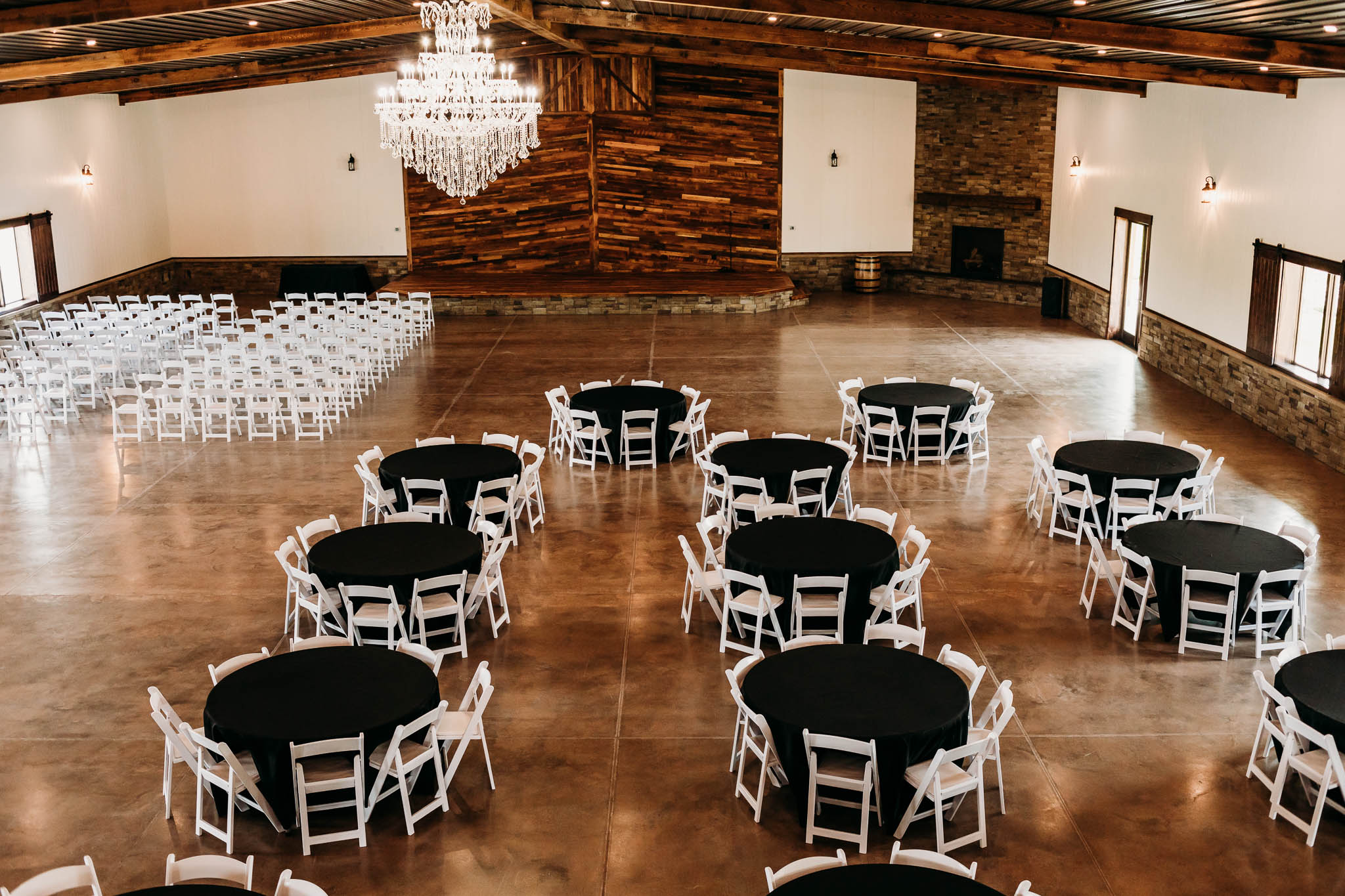 Inside The VeNue Event Space with round tables and black tablecloths set up and two columns of white vinyl chairs