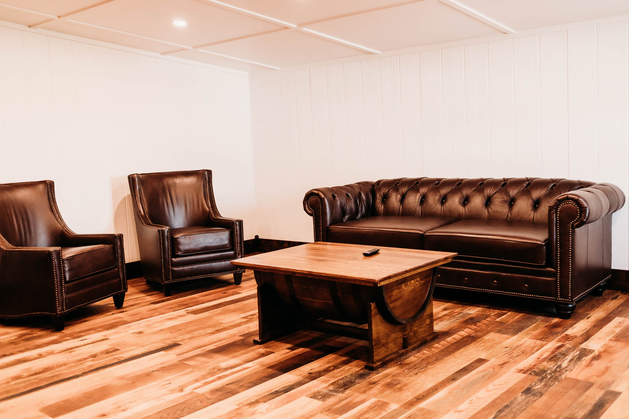 Groom's private getting ready suite at The VeNue Event Space includes a brown leather sofa, two brown leather chair and a handmade reclaimed oak wood coffee table.