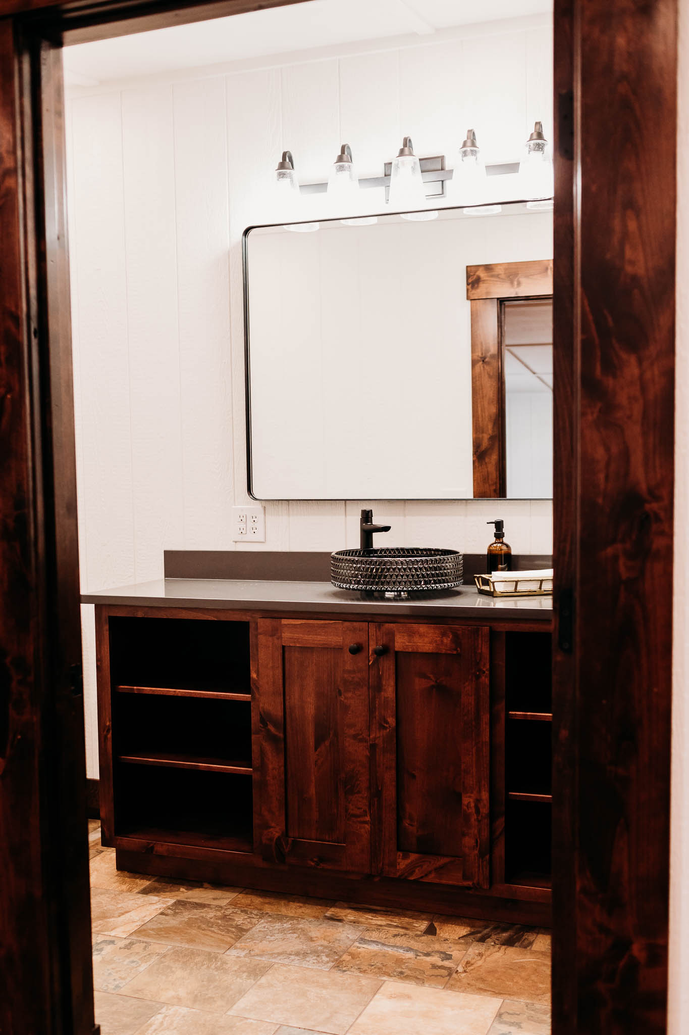 Looking into the Groom's private suite restroom where a black crystal bowl sink sits on top of the dark walnut vanity at The VeNue Event Space