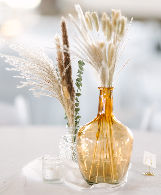 An amber colored vase with pompous grass decor and small clear vase with pompous grass and eucalyptus at The VeNue Event Space