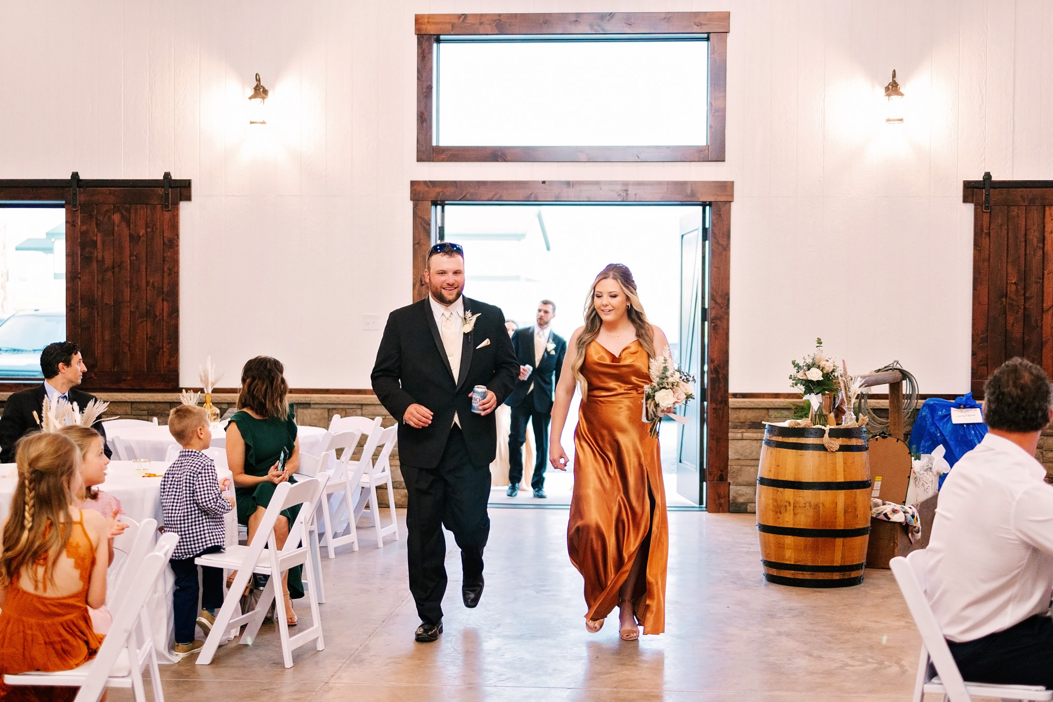 A groomsman in a black suit and bridesmaid in an orange dress enter the large front door of The VeNue Event Space