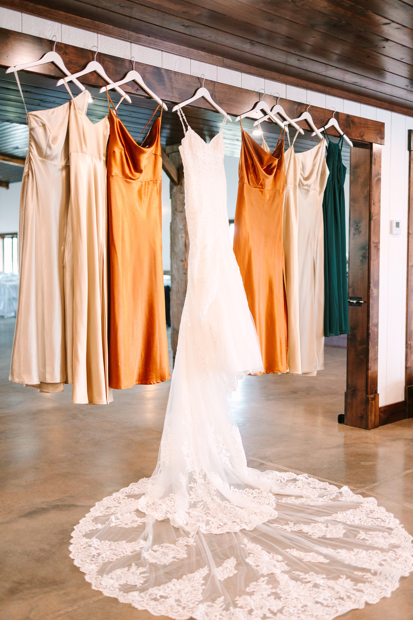 Earth toned bridesmaids dresses and a wedding dress hanging from a barn door opening at The VeNue Event Space