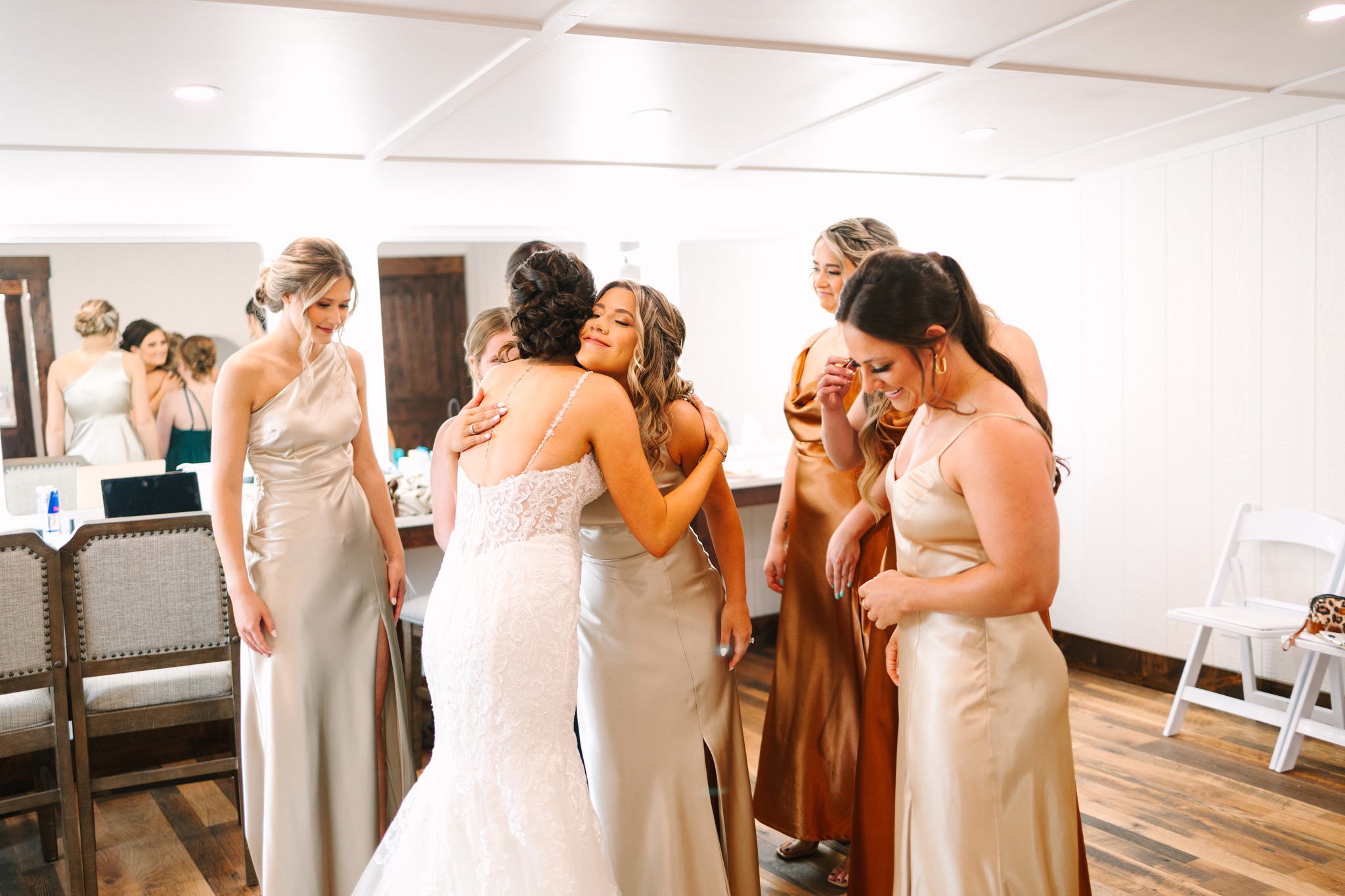 Bridesmaids in earth-toned dresses are looking at the bride and smiling and hugging at The VeNue Event Space